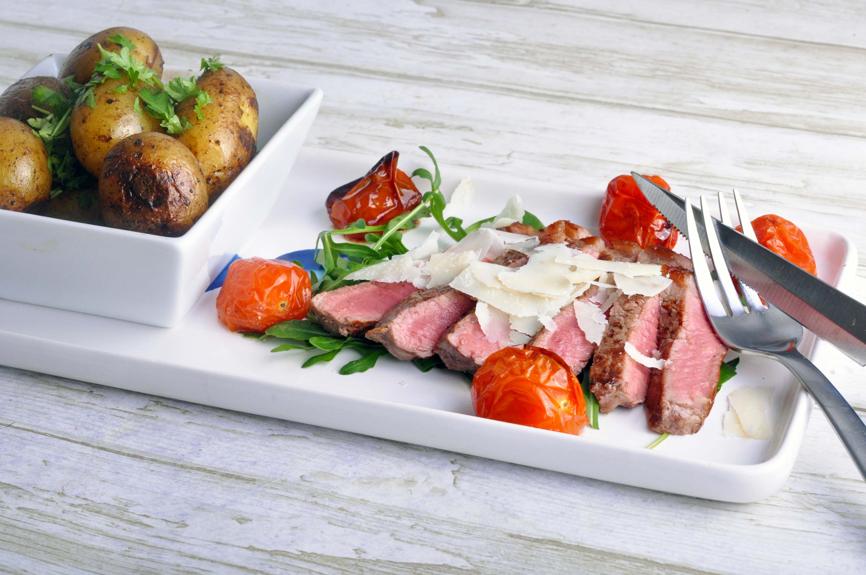 Steak with roast potatoes, baked cherry tomatoes, pesto and parmesan